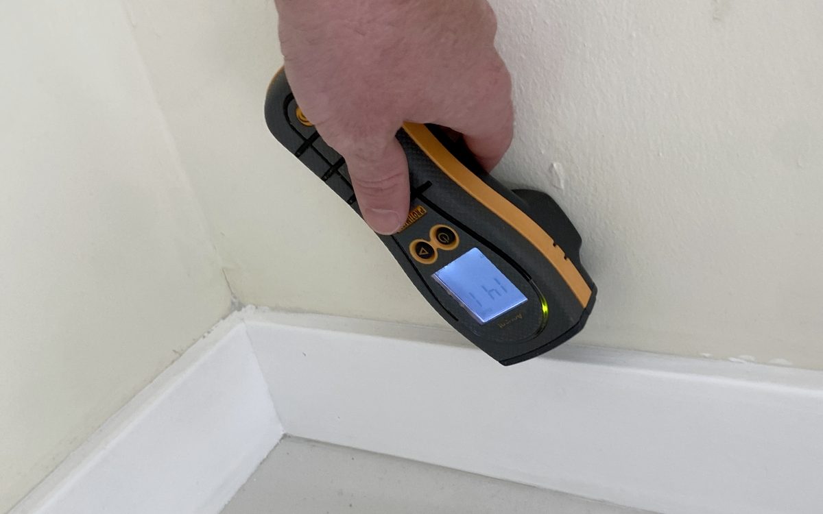 Mold inspection in Riviera Beach, FL: Moisture meter held into a baseboard corner during a mold inspection