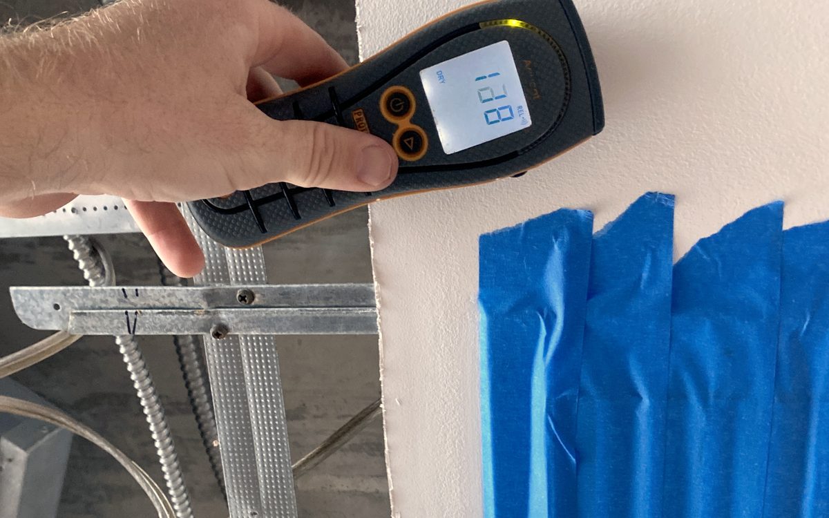 Mold inspection in Port Salerno, FL: Moisture meter used beside taped containment sheeting during an inspection