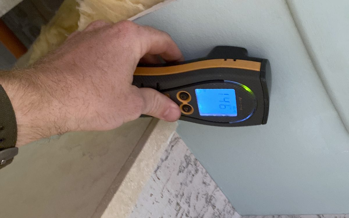 Mold inspection in Davie, FL: Moisture meter held to a ceiling edge beside exposed insulation