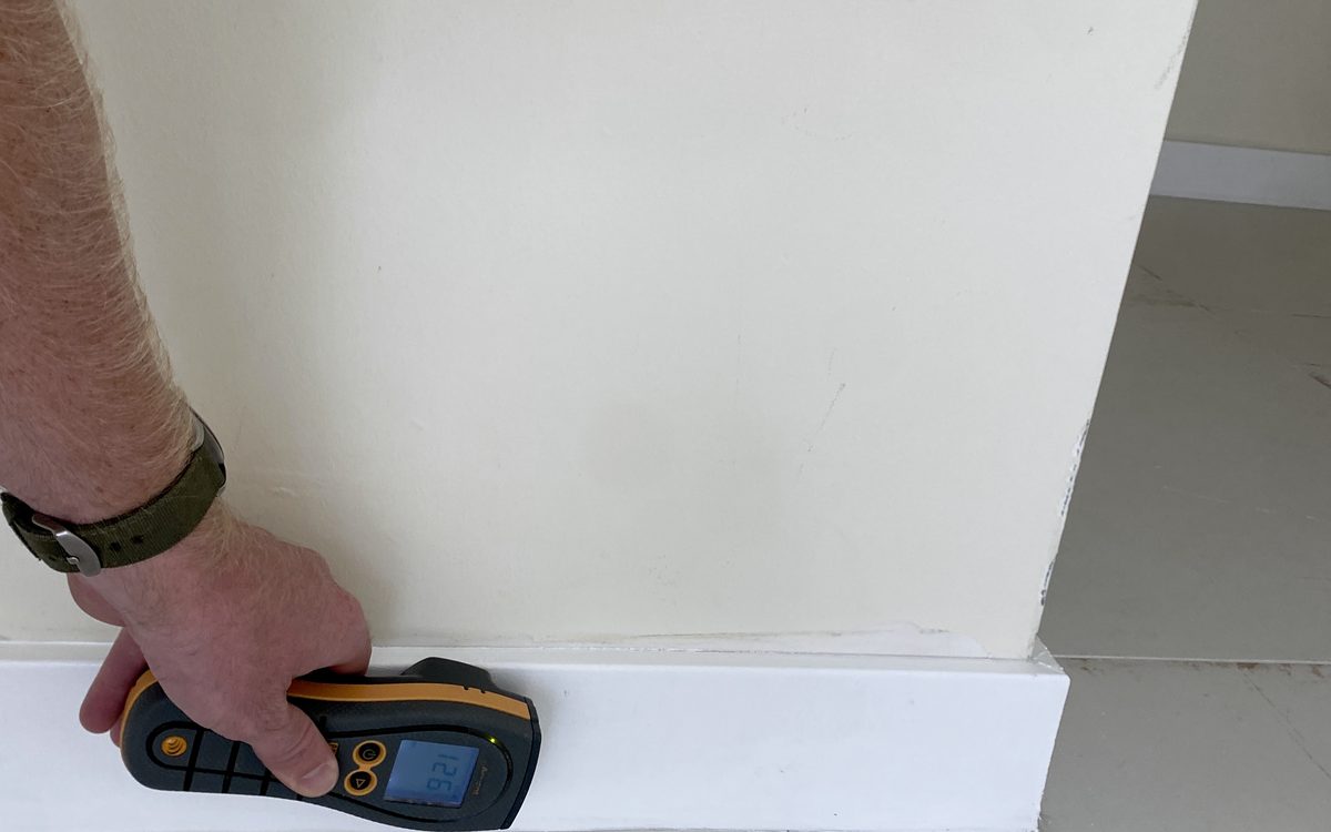Mold inspection in Deerfield Beach, FL: Moisture meter run along a painted baseboard during an inspection