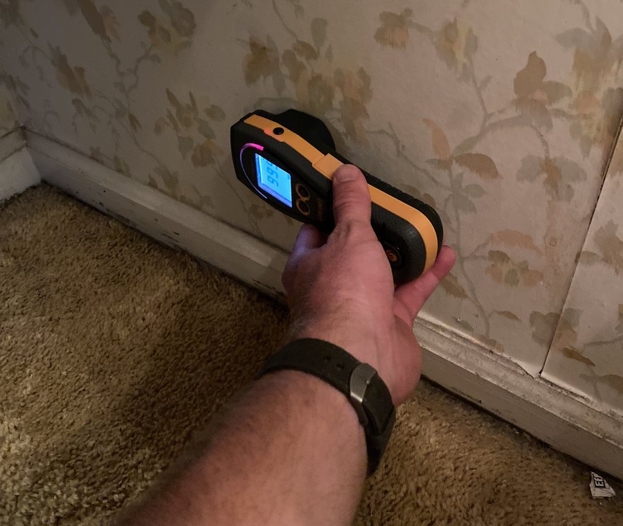 Moisture meter pressed against a wall above the baseboard in an older Florida home.
