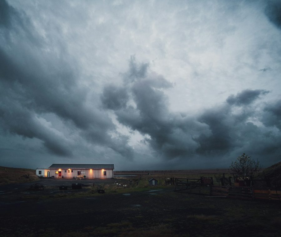 Dark storm clouds gathering over a lit house at dusk.