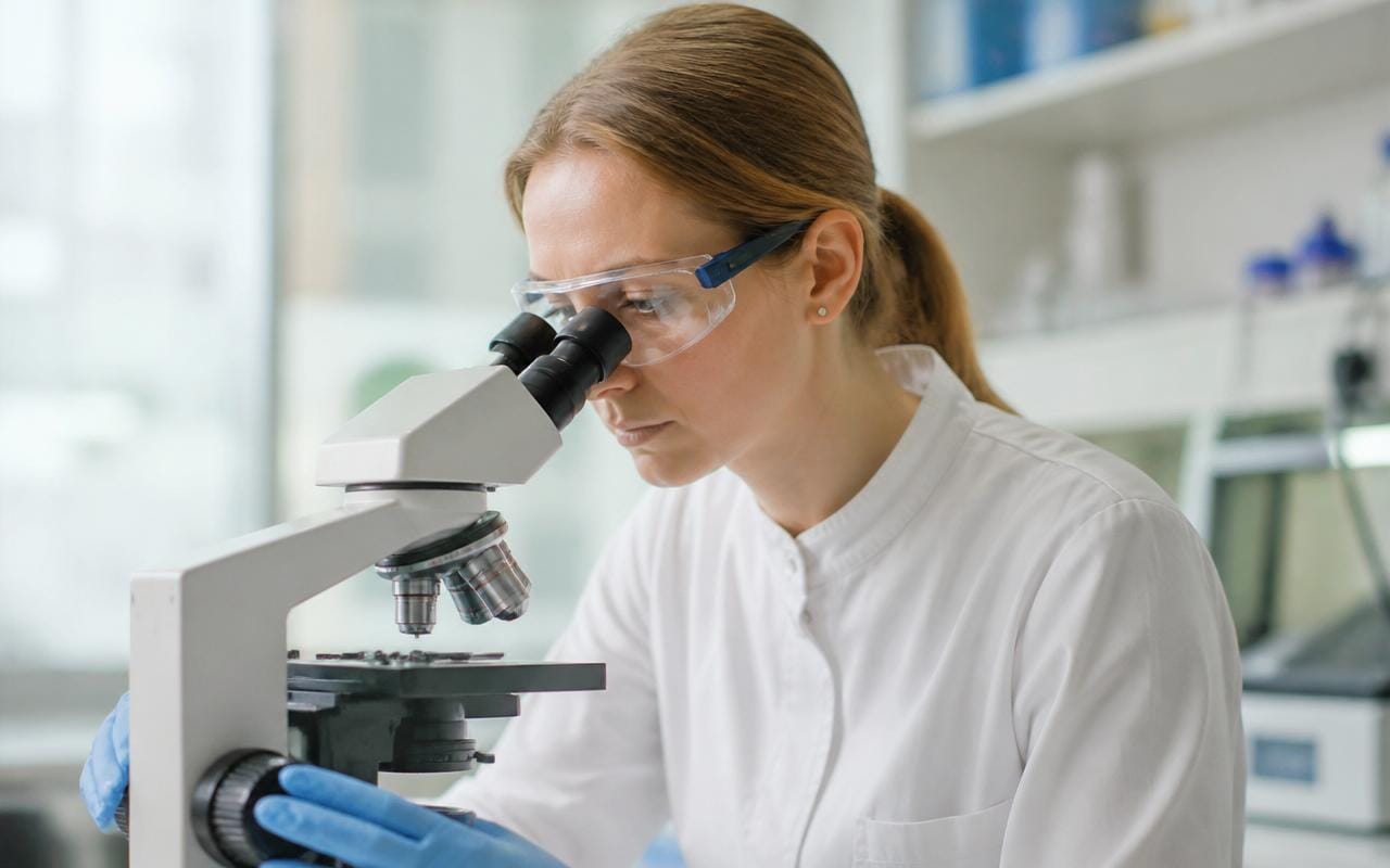 AIHA-accredited lab technician analyzing a mold sample on a microscope slide in a professional laboratory.