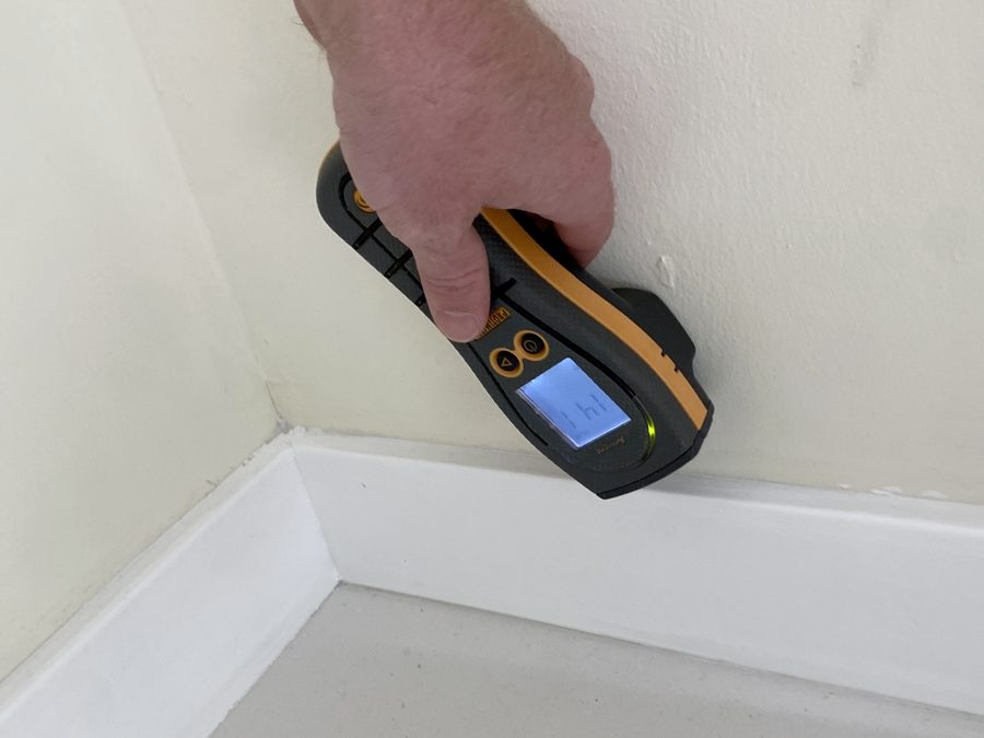 Pinless moisture meter held against a baseboard during an inspection