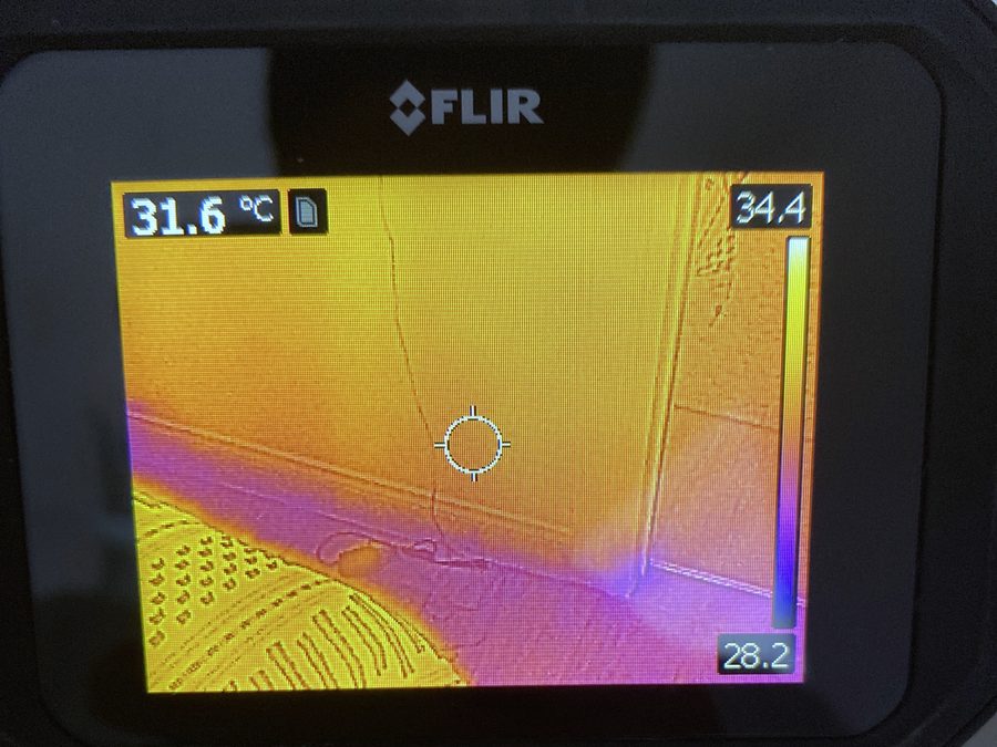 Handheld infrared camera showing a thermal image of an interior wall